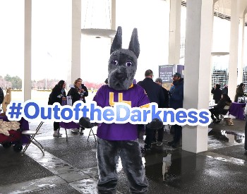 Damien the University at Albany mascot holding a "out of the darkness" sign.