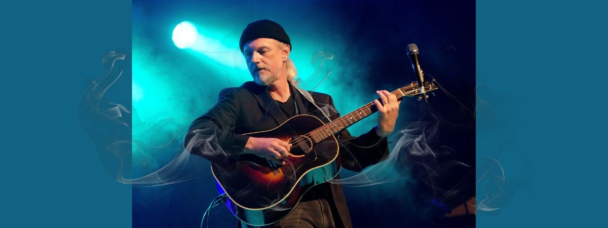 photo of Garnet Rogers onstage with a guitar under a spotlight