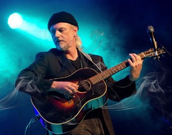 photo of Garnet Rogers onstage with a guitar under a spotlight
