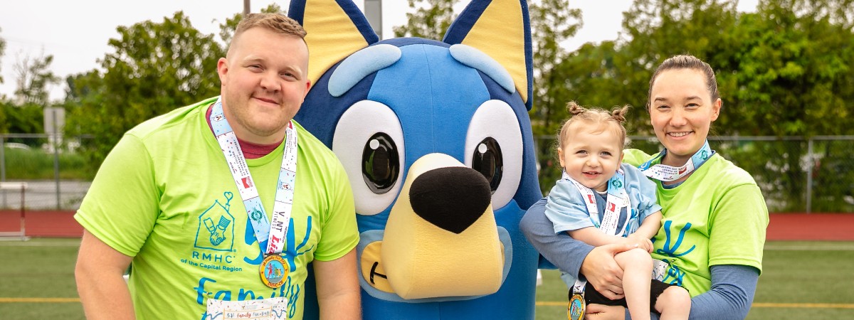 5K participants, wearing race medals and holding young girl. Family is accompanied by Bluey character.
