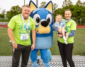 5K participants, wearing race medals and holding young girl. Family is accompanied by Bluey character.