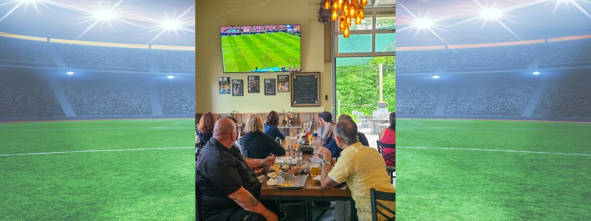 Watch World Cup soccer in Saratoga Springs at Artisanal Brew Works. This photo shows guests enjoying a match on a 100-inch screen alongside great food, refreshing beverages, and views of the surrounding forest.