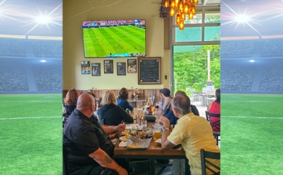 Watch World Cup soccer in Saratoga Springs at Artisanal Brew Works. This photo shows guests enjoying a match on a 100-inch screen alongside great food, refreshing beverages, and views of the surrounding forest.