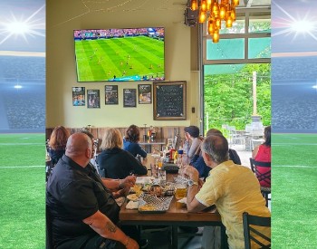 Watch World Cup soccer in Saratoga Springs at Artisanal Brew Works. This photo shows guests enjoying a match on a 100-inch screen alongside great food, refreshing beverages, and views of the surrounding forest.