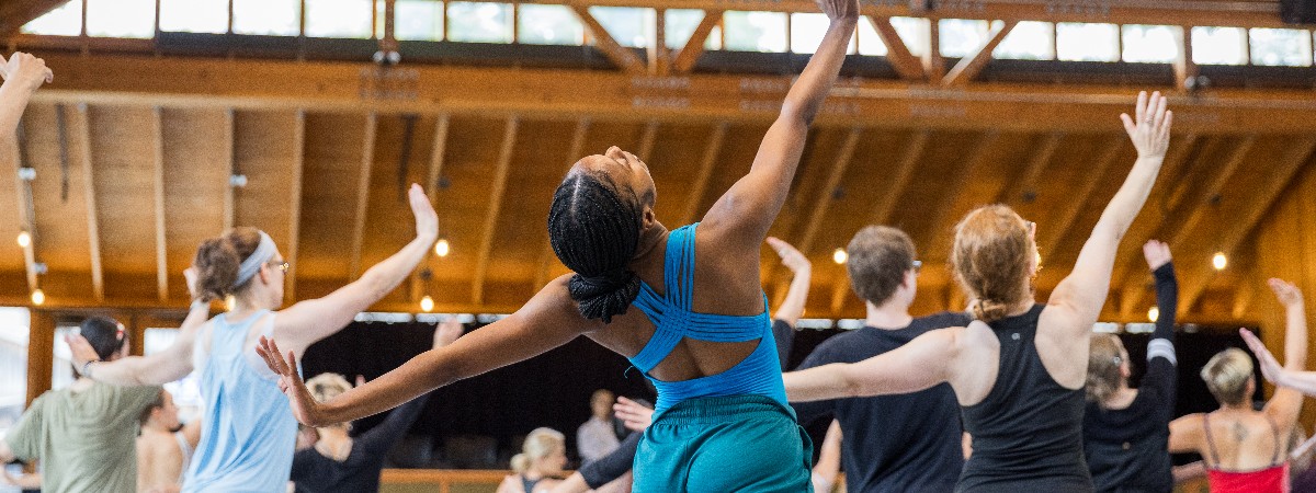 Dancers backs face the camera as they stretch their arms upwards.