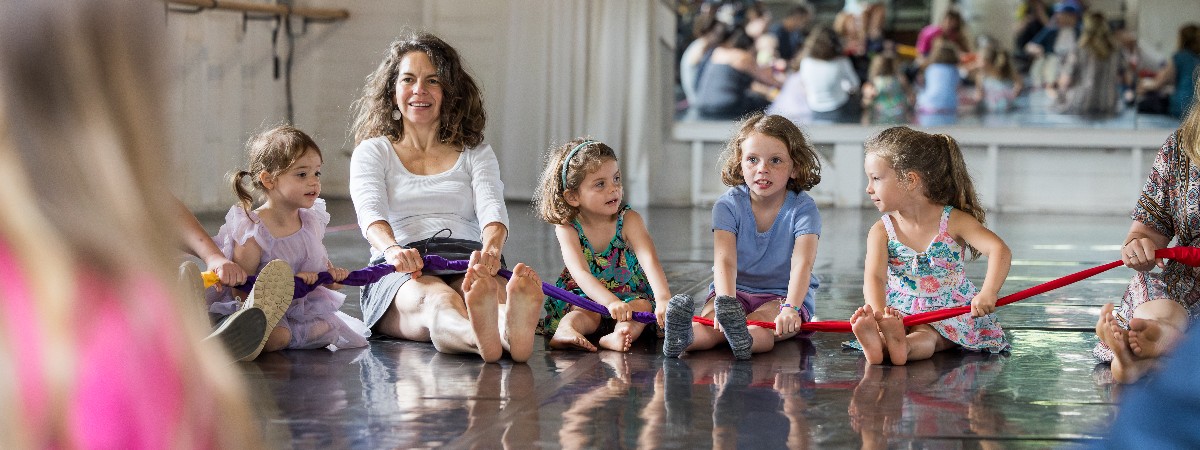 Kids sit with a teacher on the floor, holding a rope.