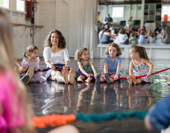Kids sit with a teacher on the floor, holding a rope.