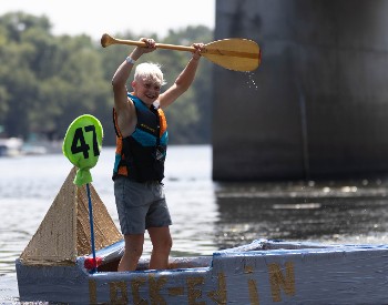 A boy holds his oar over his head in victory as he comes across the finish line during the 2025 Cardboard Boat Races.