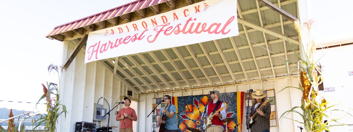 The band Ploughman's Lunch plays on a stage under an Adirondack Harvest Festival banner.