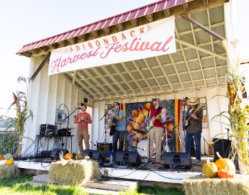 The band Ploughman's Lunch plays on a stage under an Adirondack Harvest Festival banner.