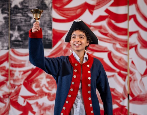 A woman in Revolutionary Era garb rings a bell