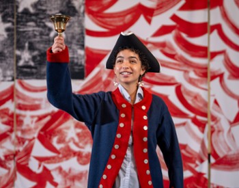 A woman in Revolutionary Era garb rings a bell