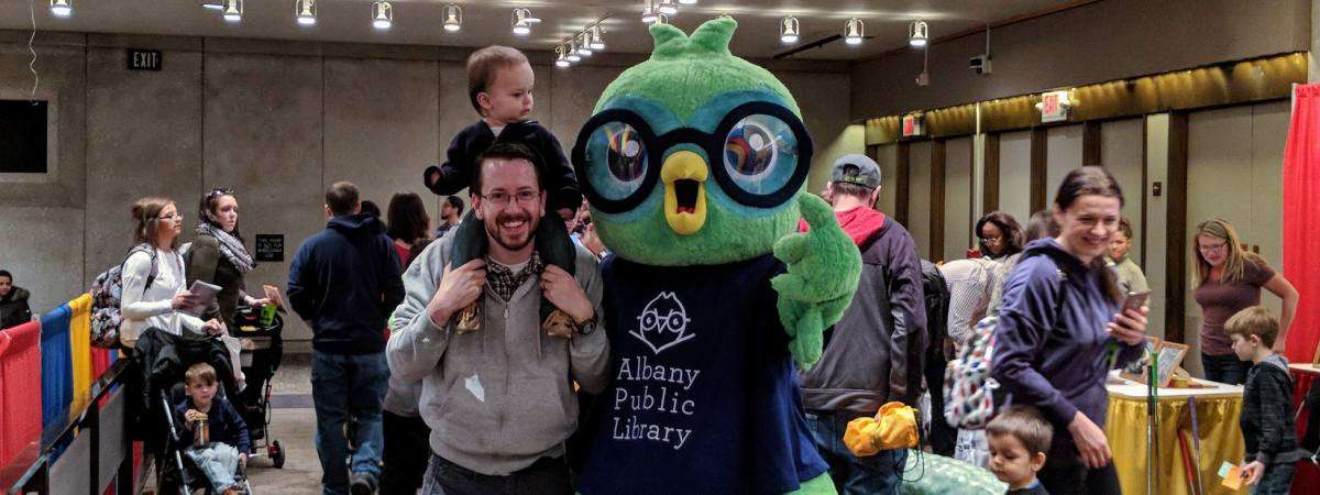 dad and toddler pose with albany public library bird mascot