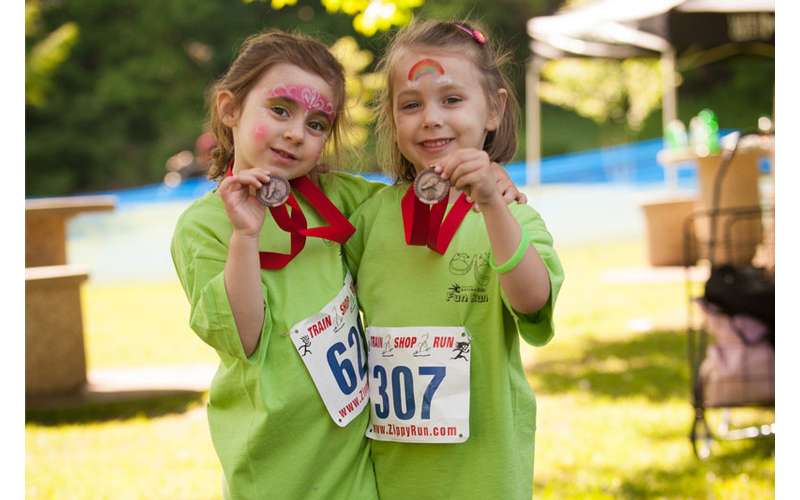 two young girls smiling and holding up race medals