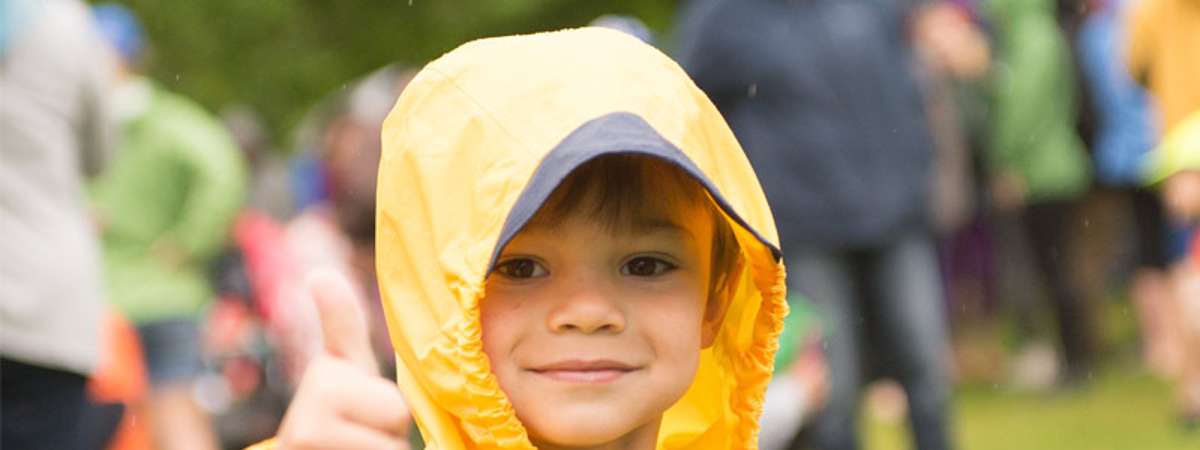 a boy in a yellow rain jacket giving a thumbs up