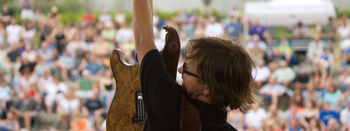 man on stage holding up guitar