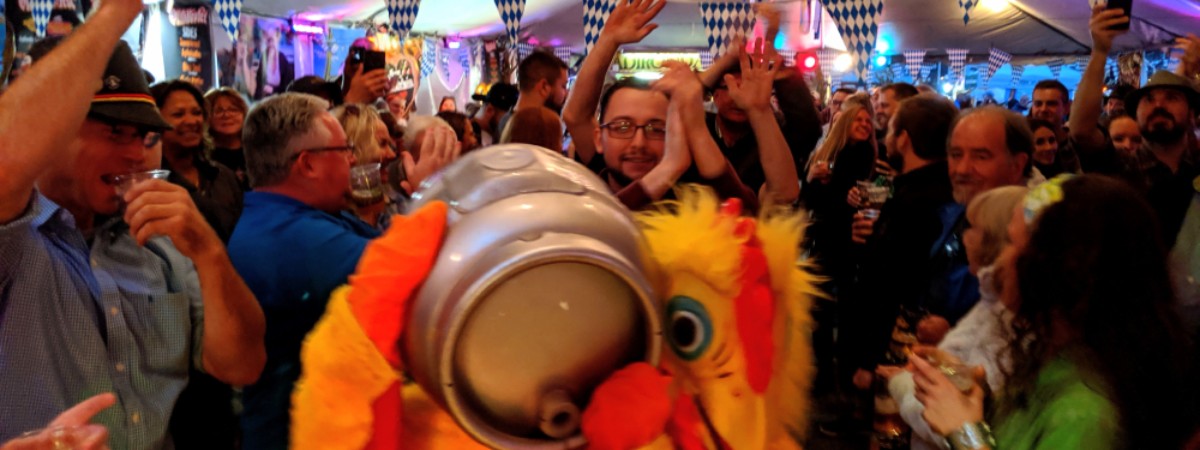 person dressed as a chicken holding up a keg in an Oktoberfest tent