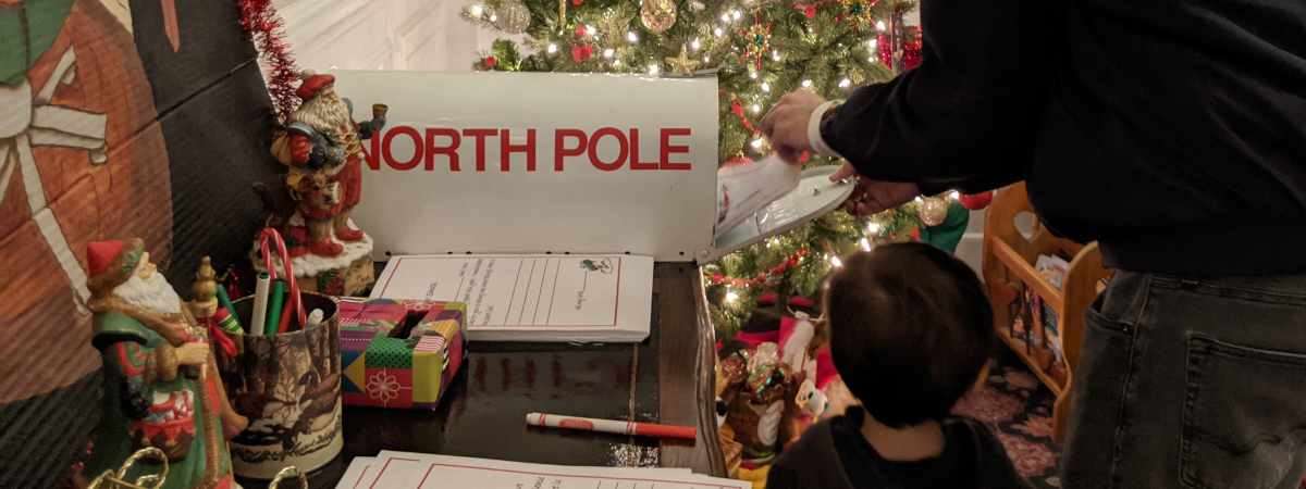 closeup of kid and dad putting a letter in a mailbox marked north pole