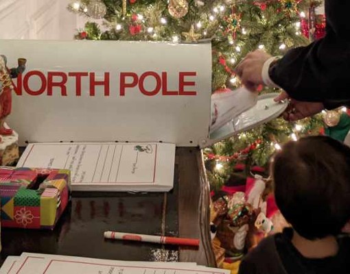 closeup of kid and dad putting a letter in a mailbox marked north pole