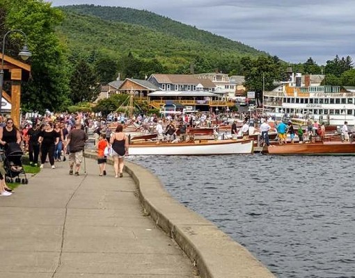 people walking along promenade by water and antique boat show