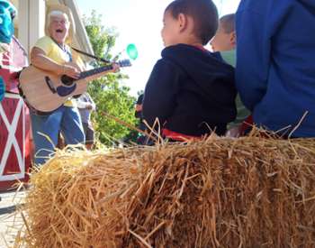 Woman plays acoustic guitar to children and families at Clifton Park Farm Fest