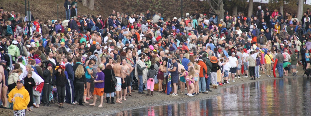 large crowd of people standing along a shoreline for a polar plunge