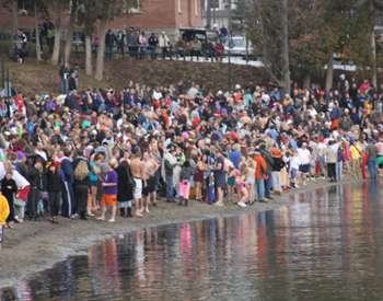 large crowd of people standing along a shoreline for a polar plunge