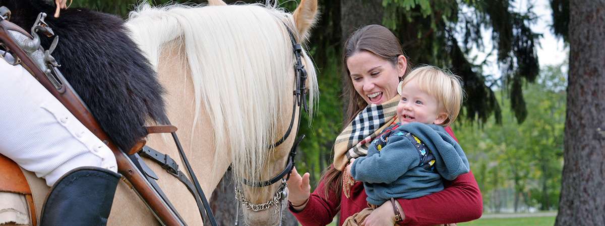 woman holding a child petting a horse