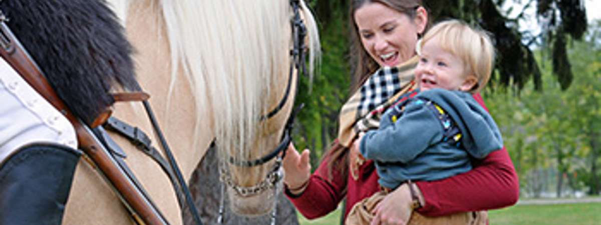 woman holding a child petting a horse