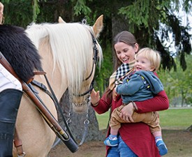 woman holding a child petting a horse