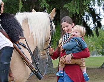 woman holding a child petting a horse