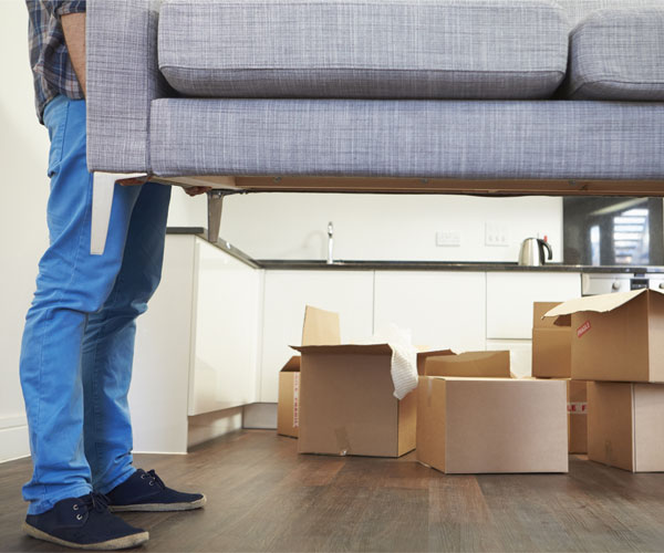 person moving a couch with cardboard boxes in the background