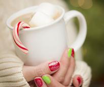 hands with red and green nails holding cocoa with candy cane
