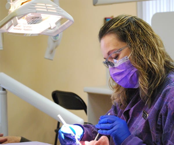dental hygienist in purple scrubs working on a patient's teeth