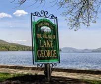 welcome to the village of lake george sign by the water