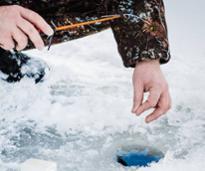 closeup of man sticking fishing line down hole in ice