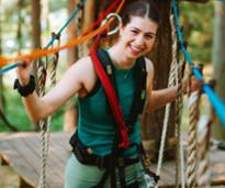 happy young woman poses on treetop course bridge