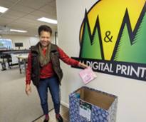 woman puts book donation in box by m and m digital printing sign