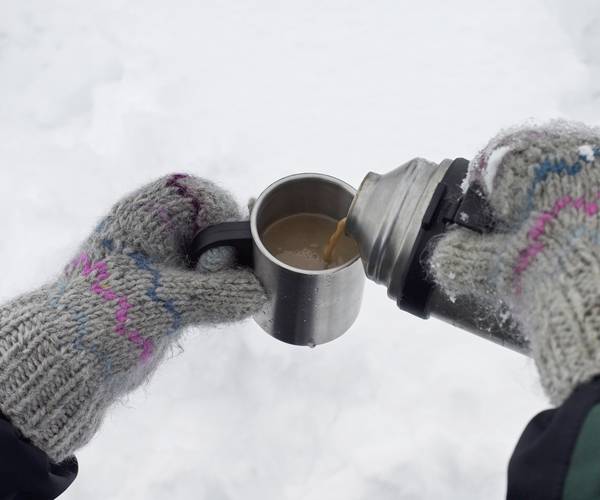gloved hands pouring warm drink from thermos