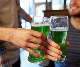two glasses of green beers cheersing