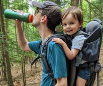 man drinking from water bottle, son on back