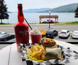 sandwich wrap and drink on outdoor table, lake in background