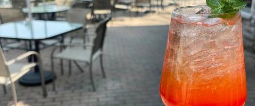 bright cocktail held up with patio dining tables in the background