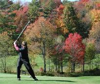 Man swinging golf ball with fall foliage in the background
