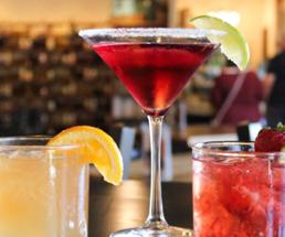 three cocktails, middle one tall, on a bar