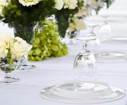 upside-down plate with upside-down glass on top, on a white tablecloth with white and green flowers on the table