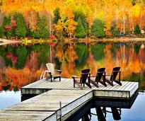 adirondack chairs on a dock with fall foliage in the background