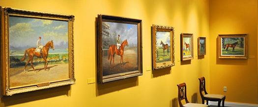 paintings of horses hung on a yellow wall