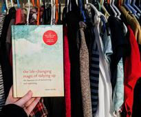Marie Kondo book held up in front of clothes in closet