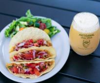 three tacos with artisanal brew works beer on patio
